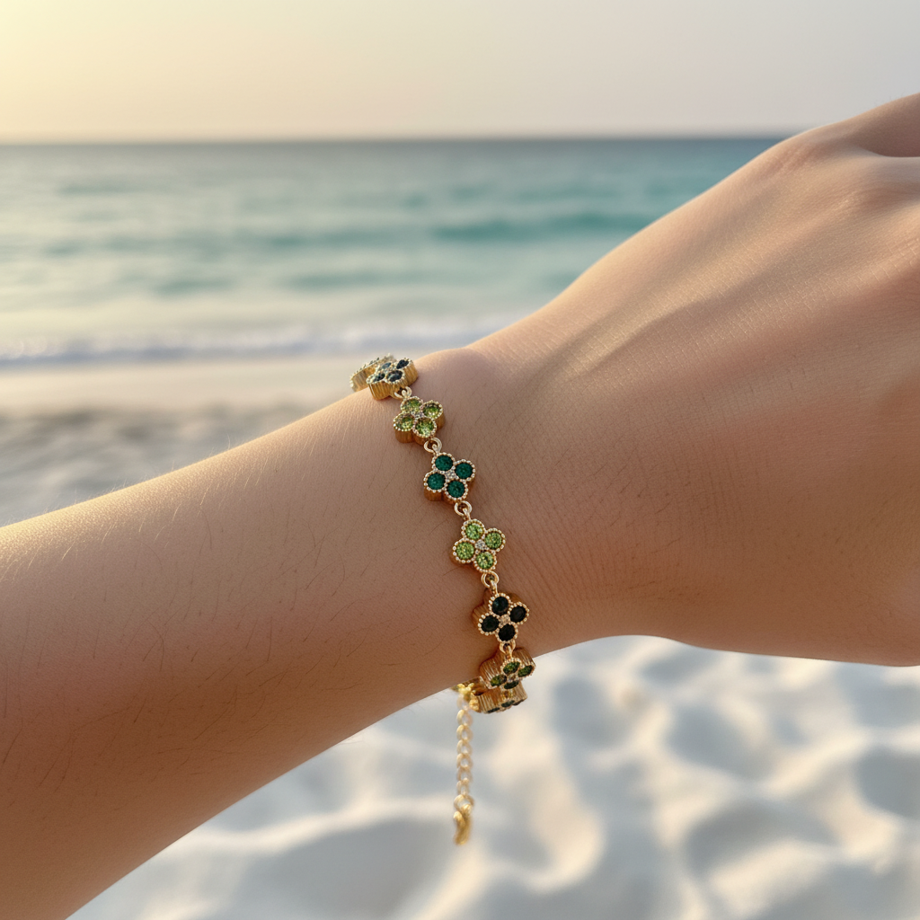 Bracelet chaîne dorée maillons trèfles pavé cristaux vert émeraude & péridot alternés – lifestyle plage